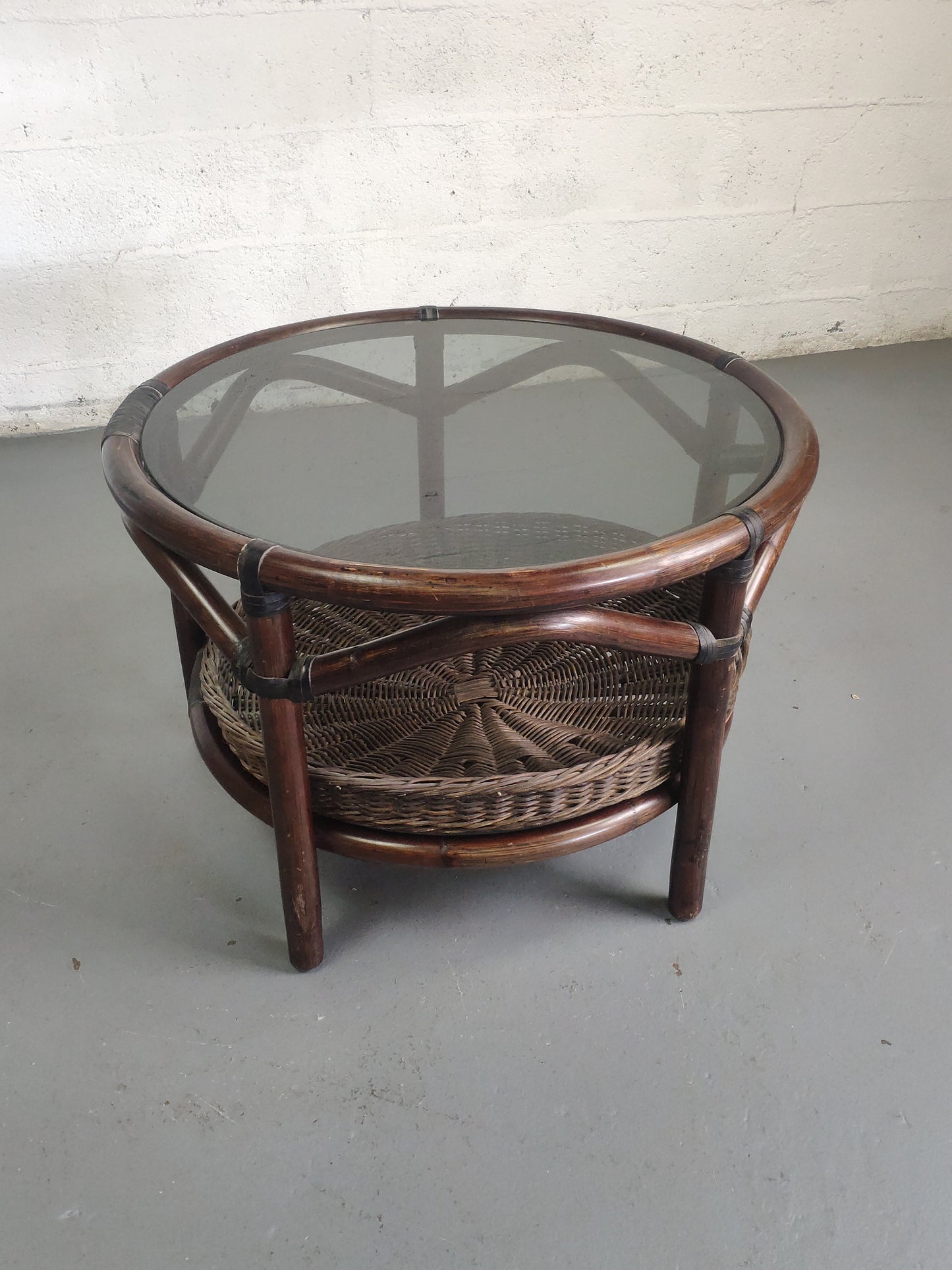 Table basse vintage en rotin avec le plateau en verre fumé et étagère panier en rotin.