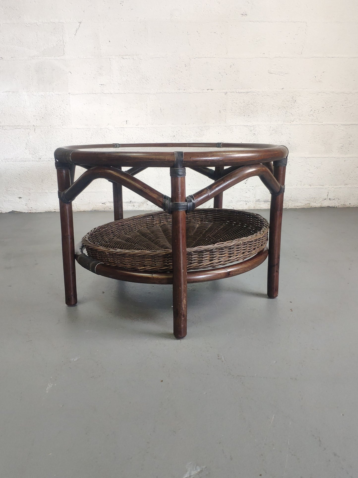 Table basse vintage en rotin avec le plateau en verre fumé et étagère panier en rotin.