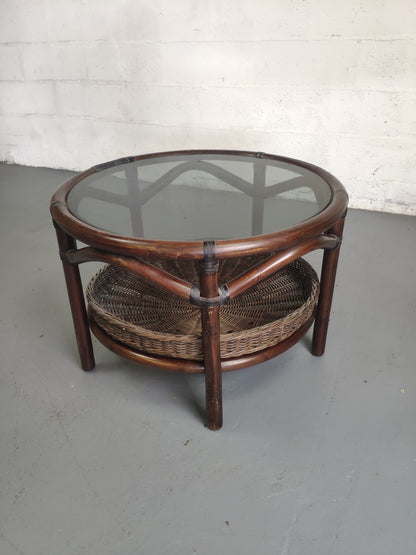 Table basse vintage en rotin avec le plateau en verre fumé et étagère panier en rotin.